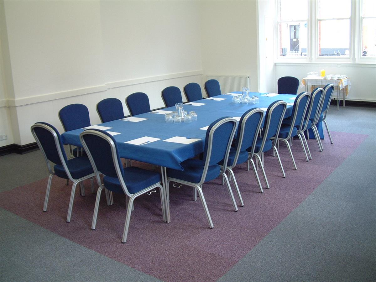 tables and chairs set up for a meeting in a wide room with a big window at one end